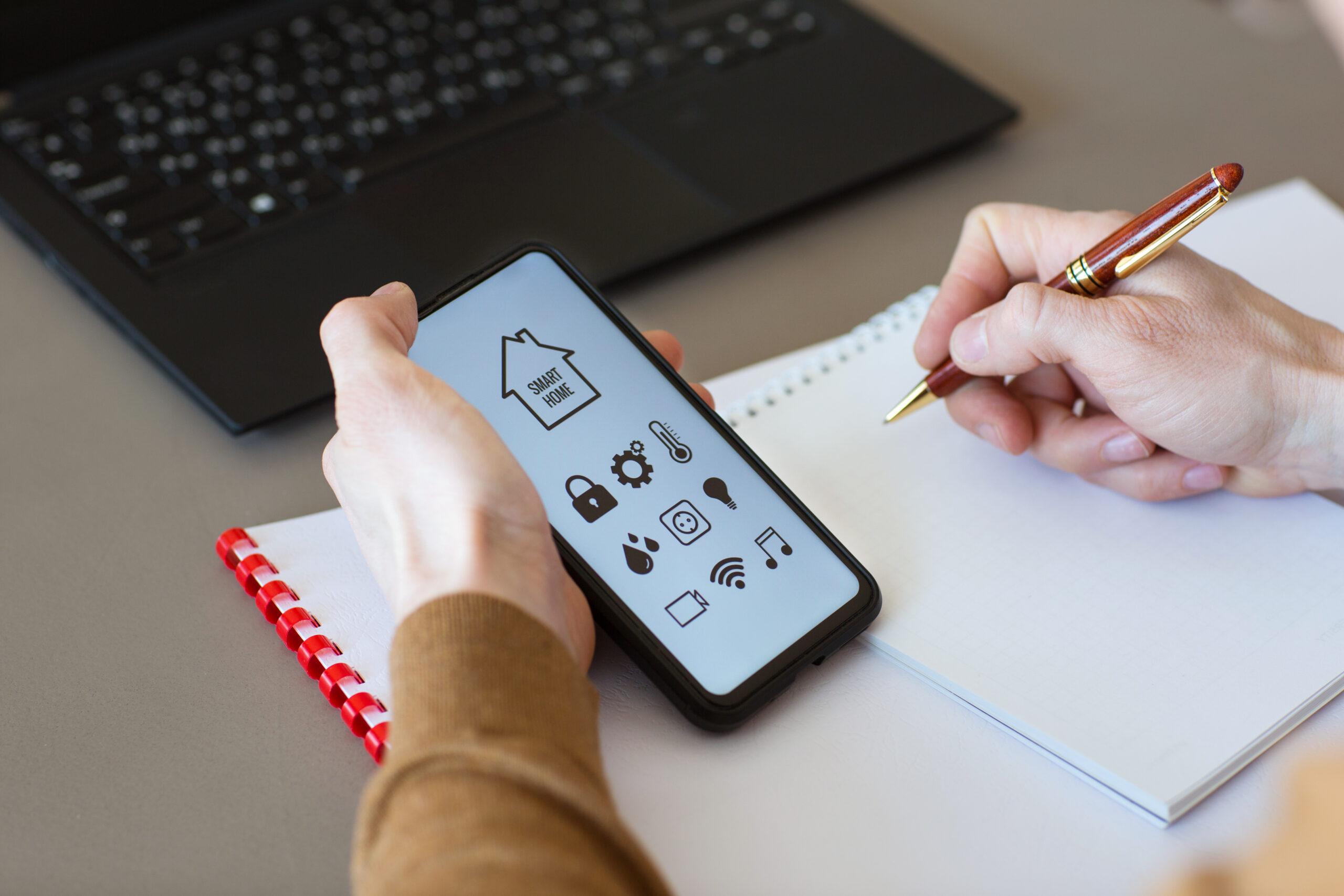 man controls smart home devices using app for mobile phone on background of businessman's work table, interior of home office. concept of digitalization. a mockup with hand holding phone